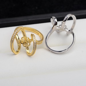 Puede incluir: Dos anillos ajustables con un engaste en forma de flor para una perla o una piedra preciosa. El anillo de la izquierda es de oro con piedras transparentes, y el anillo de la derecha es de plata.