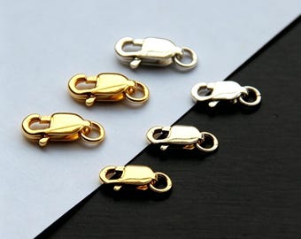May include: An assortment of gold and silver-colored lobster claw clasps. These jewelry findings are designed with a spring-loaded mechanism and a small loop for attaching to jewelry chains or other components. The clasps are displayed against a black and white background.