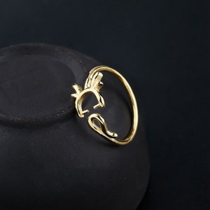 Puede incluir: Un anillo dorado con un diseño estilizado de una criatura mítica. El anillo es abierto y ajustable.