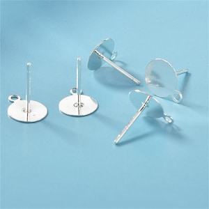 May include: Four silver earring posts with round flat backs and a loop on the side. The posts are designed for attaching earrings.