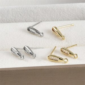 May include: A set of six earring findings with a silver and gold finish. Each finding has a small, clear crystal bar and a loop for attaching earrings.