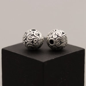 May include: Two silver beads with intricate swirling patterns. The beads are round and have a hole through the center.
