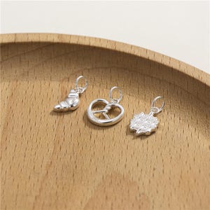 May include: Three silver charms in the shape of a croissant, pretzel, and waffle.