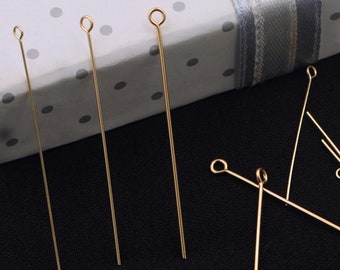 May include: Gold-colored head pins with a loop at the top. The pins are arranged on a white surface with black polka dots.