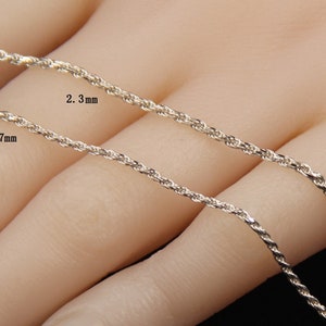 May include: Close-up of two silver-colored rope chains. One chain is labeled 1.7 mm, and the other is labeled 2.3 mm. The chains are displayed against a neutral background, highlighting their texture and design. The chains are likely for necklaces or bracelets.