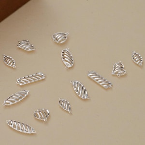May include: A collection of silver-colored metal jewelry components in various shapes including ovals, rectangles, and hearts. Each piece features a distinct diagonal slatted or ribbed design with small loops at the ends for attachment.