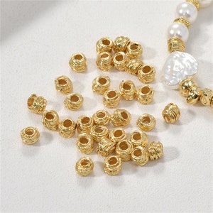 Puede incluir: Un gran grupo de cuentas espaciadoras de metal de color dorado. Las cuentas son redondas y tienen una superficie texturizada.