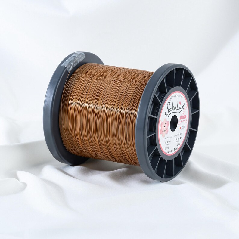 May include: A spool of copper-colored wire. The wire is tightly wound around a dark gray plastic spool. The label on the spool reads "SakuLuz" and includes details about the wire's composition and dimensions.