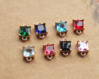 May include: Eight square gemstone charms in a variety of colours, including green, blue, turquoise, red, clear, pink, black, and light pink. Each charm is set in gold-coloured metal with a small loop for attachment.