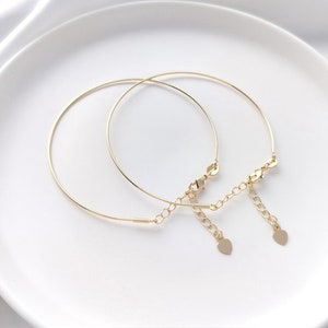 Może przedstawiać: Dwa delikatne złote bransoletki z wiszącymi serduszkami. Bransoletki są połączone małym łańcuszkiem.