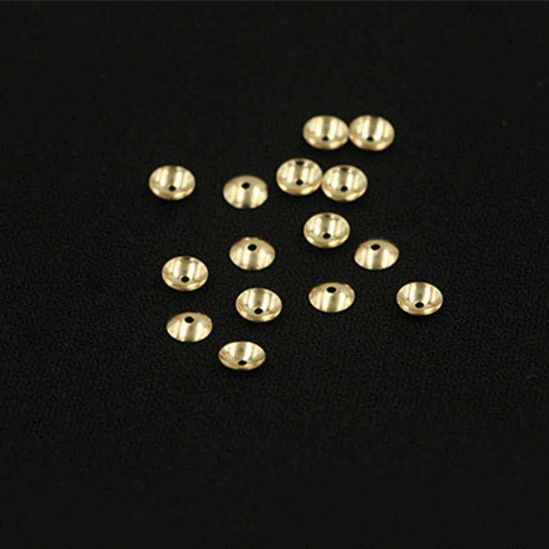 May include: A group of 16 gold-colored metal bead caps. The caps are round and have a flat top with a small hole in the center.