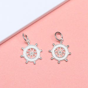 May include: Two silver ship wheel charms with a white center and a silver loop at the top.