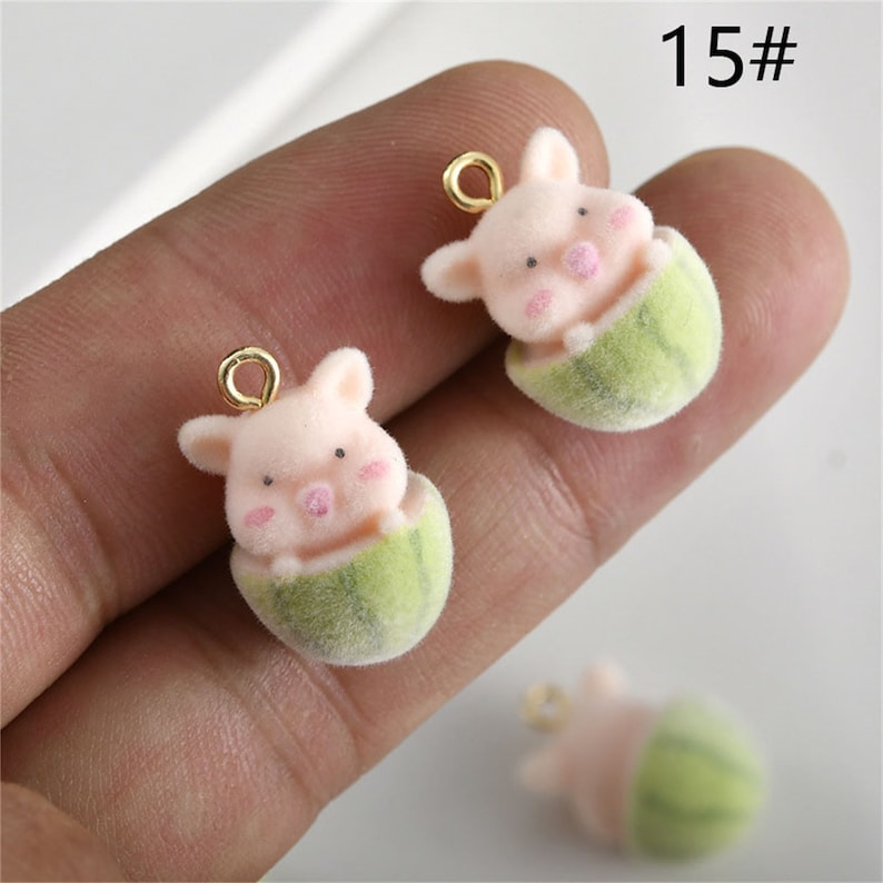 May include: Two pink pig charms with gold jump rings. Each pig is peeking out of a green watermelon charm.