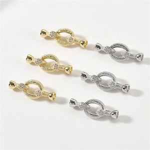 May include: Six decorative jewelry clasps. Three are gold-toned with clear crystal accents, and three are silver-toned with similar crystal accents. Each clasp features a textured oval center and a cylindrical end.