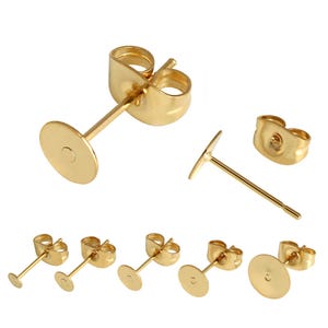 Könnte beinhalten: Eine Sammlung von Ohrstecker-Rohlingen aus goldfarbenem Metall, jeweils mit einer flachen, runden Platte zum Anbringen von Dekorationen und einem dünnen Stift. Das Set enthält mehrere einzelne Ohrstecker und passende Schmetterlingsverschlüsse.