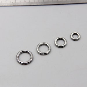 Könnte beinhalten: Drei silberfarbene Metallringe mit einer texturierten, gedrehten Seiloptik, die nach Größe in einer Reihe angeordnet sind und unter einem Metalllineal mit Zentimeterangaben liegen, um eine klare Skala für die Schmuckteile zu bieten.