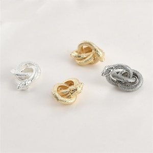 May include: Four metal snake figurines in silver and gold tones are arranged on a white surface. The snakes are coiled, with detailed scales and heads. The figurines vary in size and design, showcasing a variety of textures.