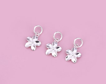 May include: Three silver flower charms with a loop at the top for attaching to jewelry. The charms are in the shape of a five-petal flower.