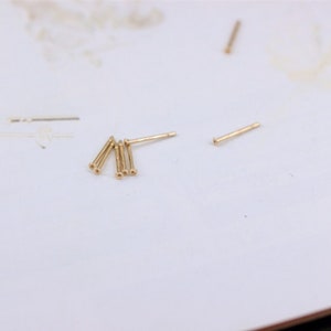 May include: A close-up of five gold-colored metal pins on a white surface.