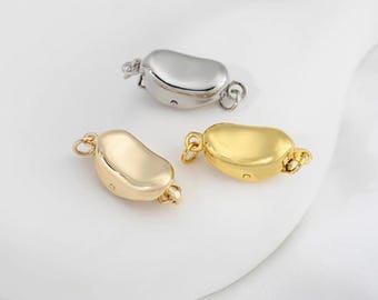 May include: Three metal jewelry clasps in gold and silver tones. The clasps have a rounded, bean-like shape with small loops on each end for attaching to jewelry. The clasps are on a white surface.