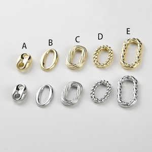 Può includere: Una collezione di elementi di gioielleria ovali in tonalità oro e argento. Gli elementi includono vari design, come superfici lisce, intrecciate e strutturate. Gli elementi di gioielleria sono esposti su una superficie bianca.