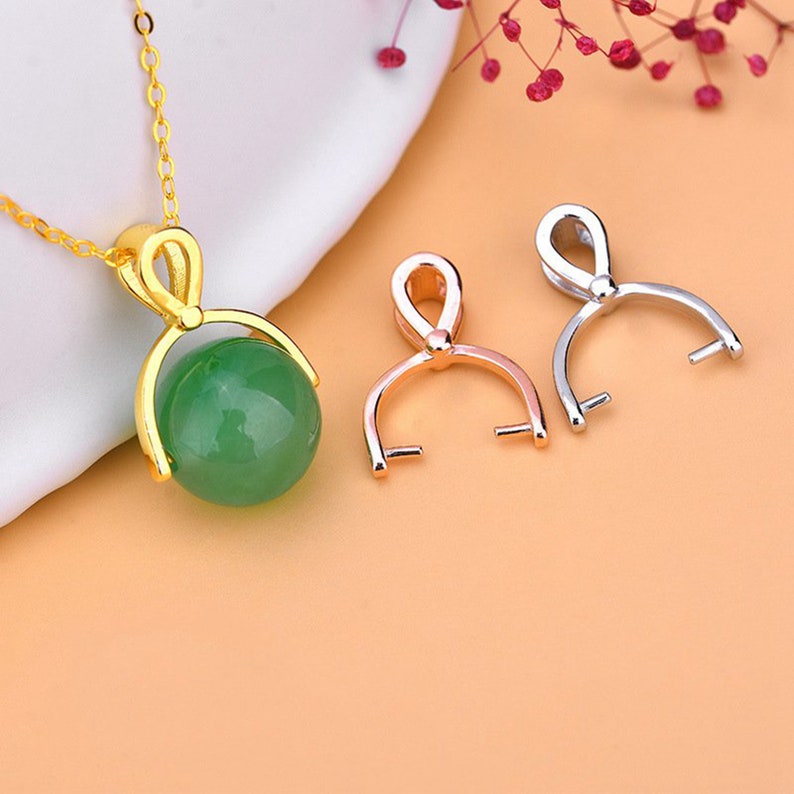 May include: A gold-colored necklace with a green jade sphere pendant. Two metal pendant holders, one rose gold and one silver, are also displayed. The necklace and pendants are set against a soft, blurred background.