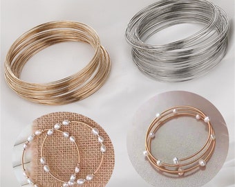 May include: Two sets of gold and silver wire bracelets. The gold bracelets are stacked on top of each other and the silver bracelets are stacked on top of each other. There are also two sets of gold bracelets with white pearls.