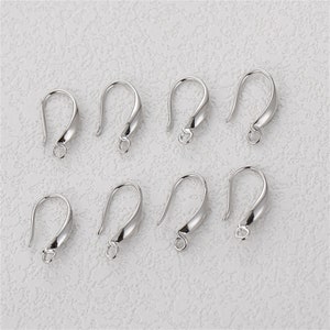 May include: Eight silver-colored earring hooks. Each hook has a curved design with a loop at the bottom for attaching beads or charms. The hooks are displayed on a textured, off-white surface.