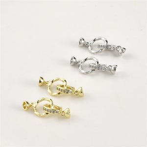 May include: Four jewelry clasps in gold and silver tones. Each clasp features a decorative ring with a smaller ring adorned with small, clear stones. The clasps have a toggle and loop design, suitable for necklaces or bracelets.