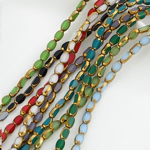 Peut inclure: Assortiment de perles de verre ovales avec une bordure dorée. Les perles sont de différentes couleurs, notamment le vert, le bleu, le rouge, le blanc et le noir.