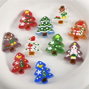 May include: A collection of colorful, miniature Christmas tree ornaments. The ornaments are in various colors, including red, green, blue, and clear, and are decorated with white accents. Each tree has a brown base.