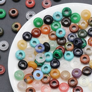 Peut inclure: Un assortiment de perles en forme de beignets en pierres précieuses colorées. Les perles sont faites de différentes pierres naturelles, notamment la turquoise, la malachite et l'améthyste. Elles sont parfaites pour la fabrication de bijoux, l'artisanat et la décoration intérieure.
