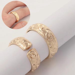 May include: Gold-coloured ring and bracelet set featuring detailed floral and swirl designs. The ring is displayed on a finger, and the bracelet is open and adjustable. The jewellery has a polished finish, reflecting light.