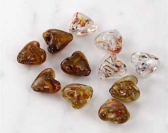 May include: Assortment of heart-shaped glass beads with gold and silver flecks. The beads are clear, amber, and brown.
