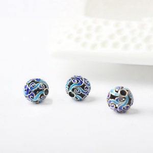 Può includere: Tre perline rotonde con un designo in smalto blu e nero. Le perline sono in argento e hanno un foro al centro per essere infilate.