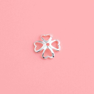 May include: Silver four-leaf clover charm with a hole in the center, perfect for jewelry making.