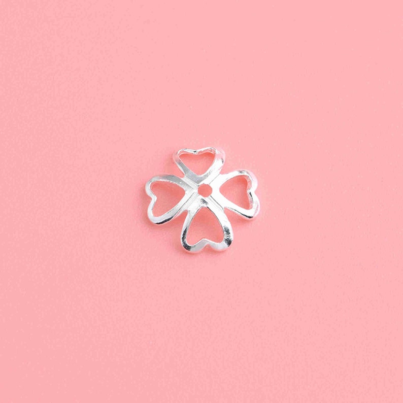 May include: Silver four-leaf clover charm with a hole in the center, perfect for jewelry making.