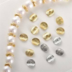 May include: Assortment of gold and silver metal bead caps. The bead caps are round with a raised center and a hole in the center. The bead caps are arranged on a white surface.