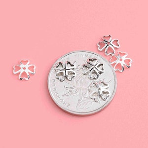 May include: Four silver-toned clover-shaped bead caps, with a Chinese coin in the background.