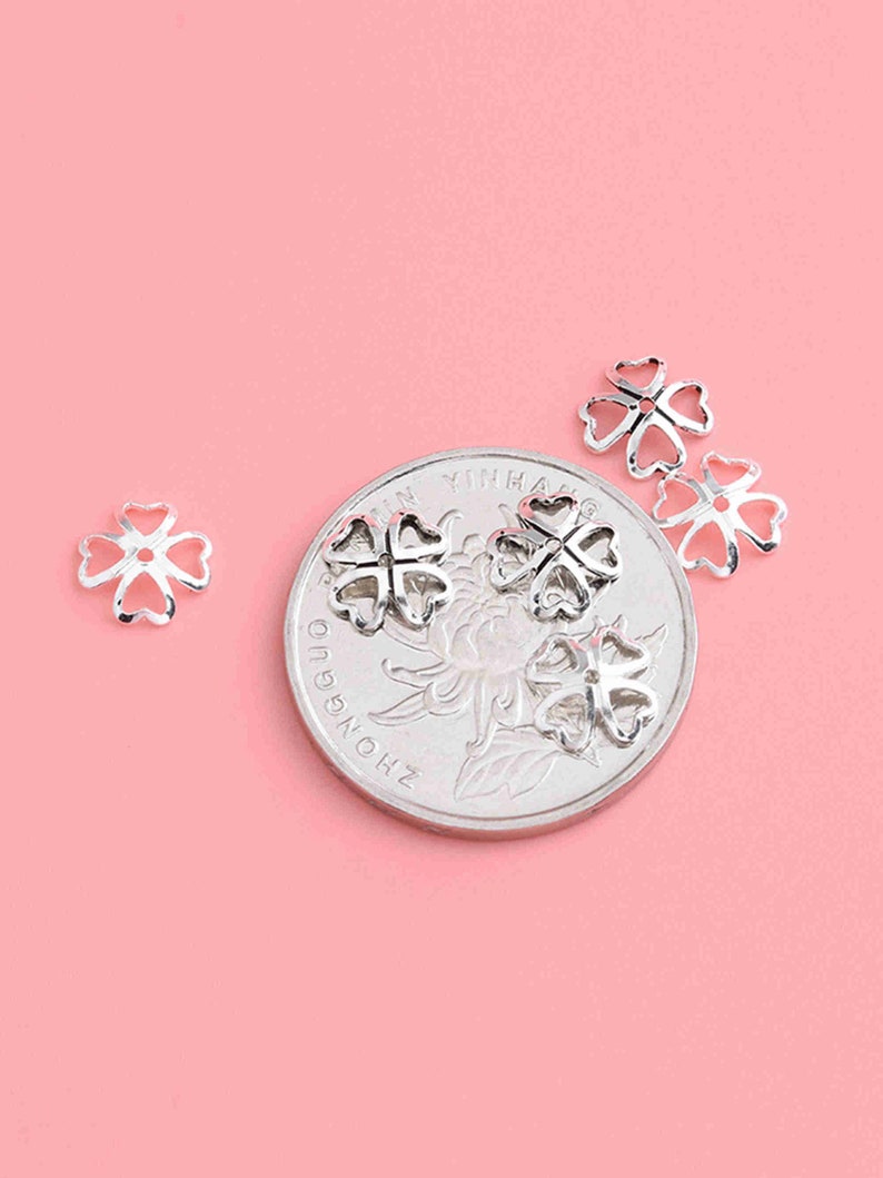 May include: Four silver-toned clover-shaped bead caps, with a Chinese coin in the background.