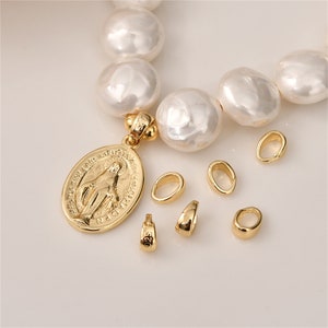 May include: A gold pendant with a religious image of the Virgin Mary, surrounded by a pearl necklace. The pendant is attached to a gold chain with a small gold clasp. There are also several small gold jump rings scattered around the pendant.
