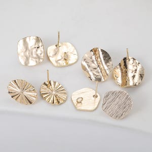 Könnte beinhalten: Eine Auswahl an goldfarbenen Ohrsteckern in verschiedenen organischen Formen. Die Ohrringe haben strukturierte Oberflächen, darunter gehämmertes und geriffeltes Design. Die Stifte sind auf der Rückseite der Ohrringe sichtbar, was auf ihren Steckerstil hindeutet. Die Ohrringe werden auf hellem Hintergrund präsentiert.