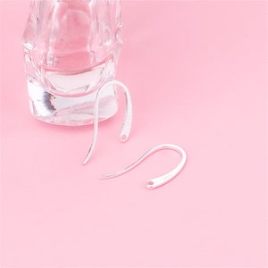 May include: Two silver earring hooks on a pink background. The hooks are made of metal and have a simple design.