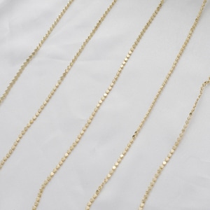 May include: Five gold chains with a square link pattern. The chains are laid out in a straight line on a white background.