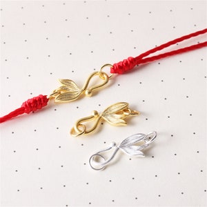 以下が含まれることがあります： 赤い紐が付いた金と銀の留め具が3つ。留め具はスタイリッシュな葉の形をしていて、片側にループ、反対側にフックが付いています。