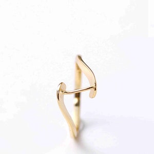 May include: A gold ring with a unique, abstract design. The ring is made of a single piece of metal that is bent and twisted to create a modern and stylish look.