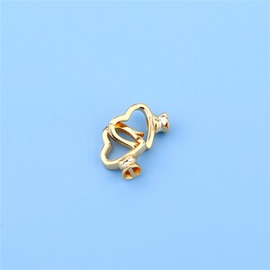 May include: Gold-toned metal heart-shaped clasp with a decorative design. The clasp is open and ready to be attached to a necklace or bracelet.