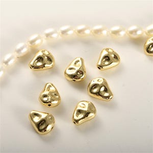 May include: A collection of eight gold-toned, irregular shaped, pearlescent beads. The beads have a textured, bumpy surface.
