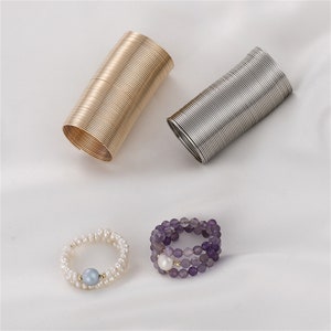Puede incluir: Tres tipos diferentes de anillos. Un anillo está hecho de un alambre de plata enrollado, otro está hecho de un alambre de oro enrollado y el tercer anillo está hecho de cuentas moradas con una perla en el centro.