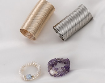 May include: Three different types of rings. One ring is made of a coiled silver wire, another is made of a coiled gold wire, and the third ring is made of purple beads with a pearl in the center.